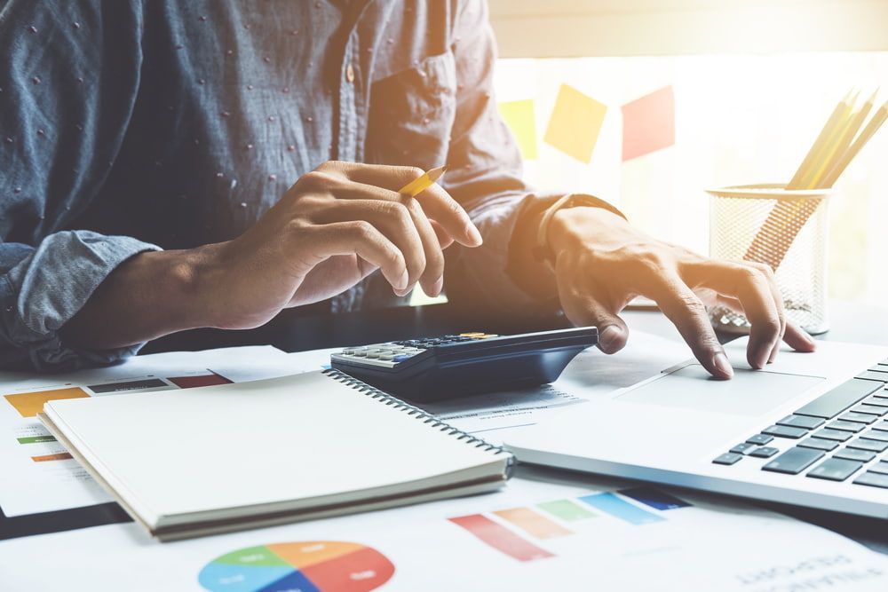 A Man is Sitting at a Desk Using a Calculator and a Laptop Computer — Pola & Co In Warrnambool, VIC