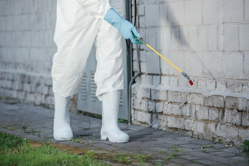 a person in a protective suit is spraying a brick wall with a sprayer .