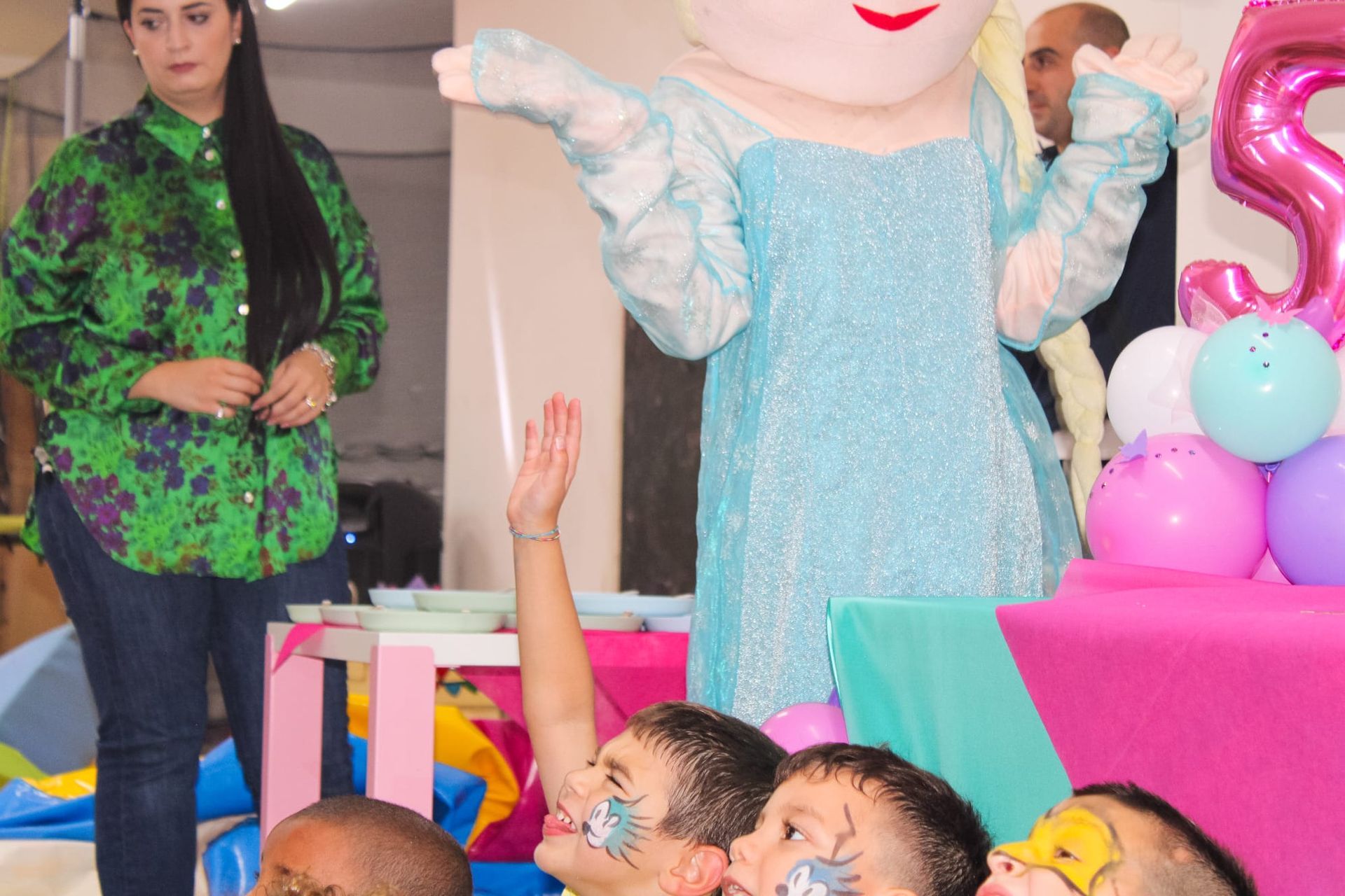 Un gruppo di bambini è seduto davanti a una mascotte vestita da Elsa di Frozen.