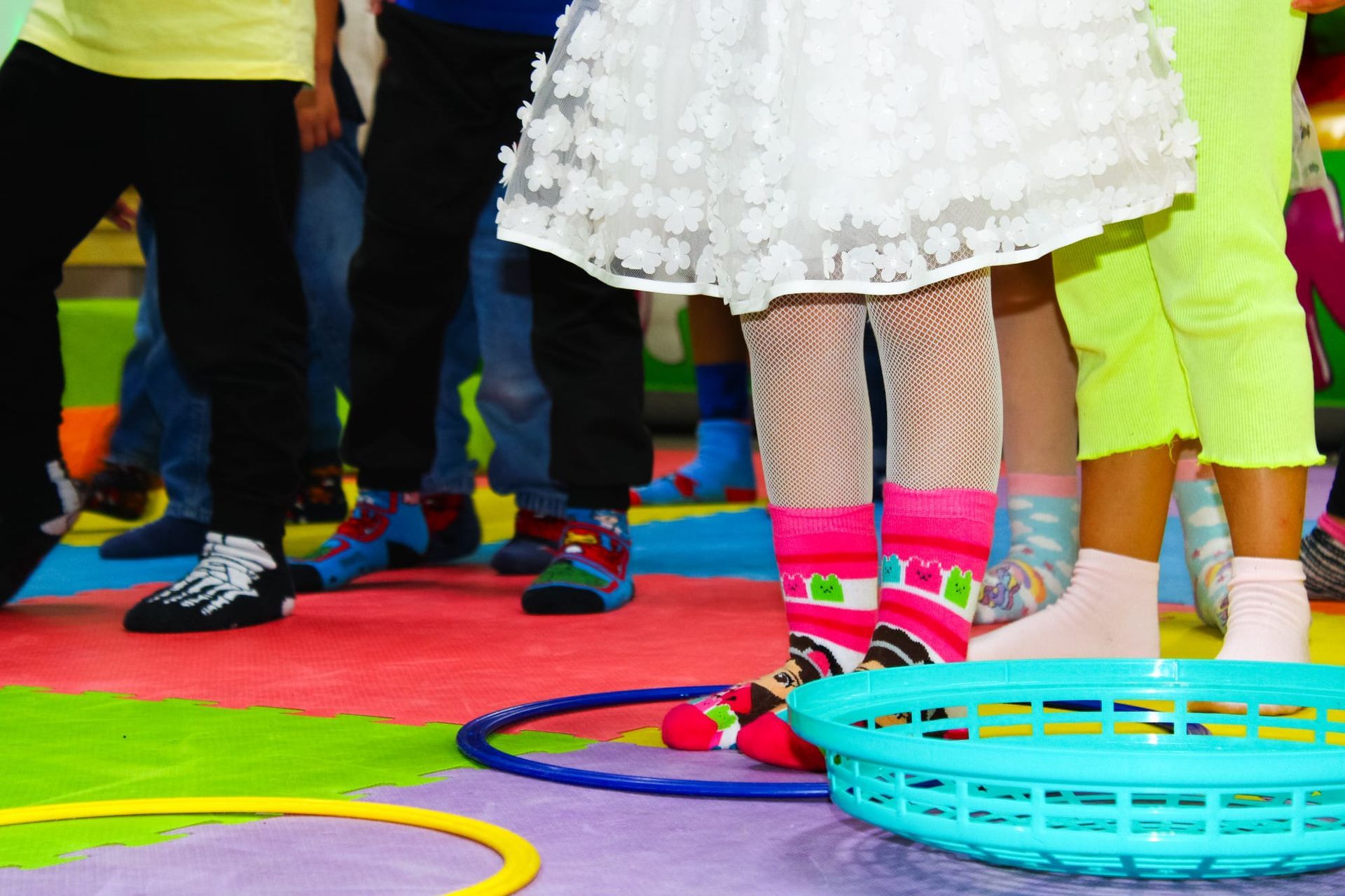 Una ragazza con un vestito bianco e calzini rosa è in piedi accanto a un cestino blu.