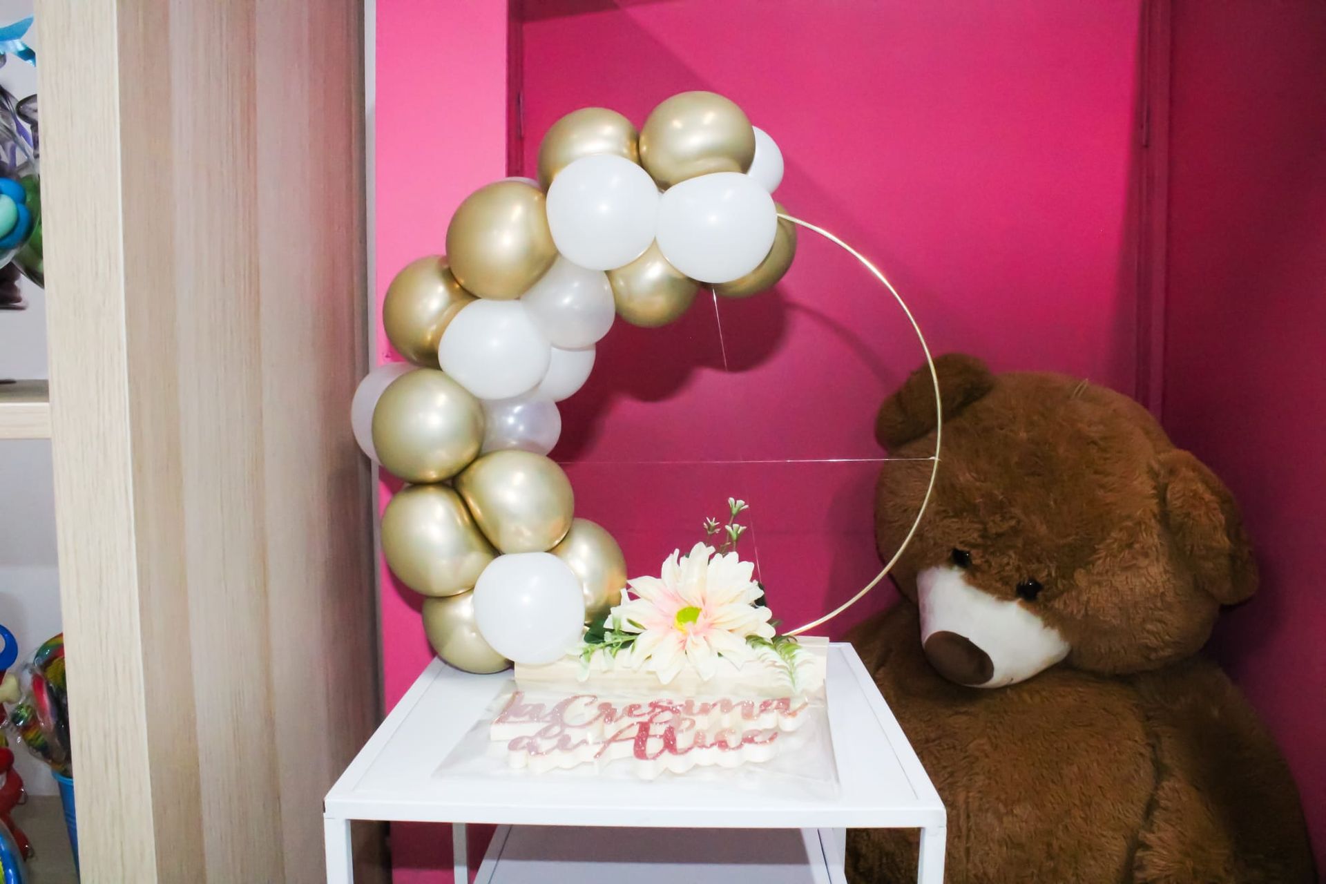 Un orsacchiotto è seduto accanto a un tavolo con palloncini e una torta.