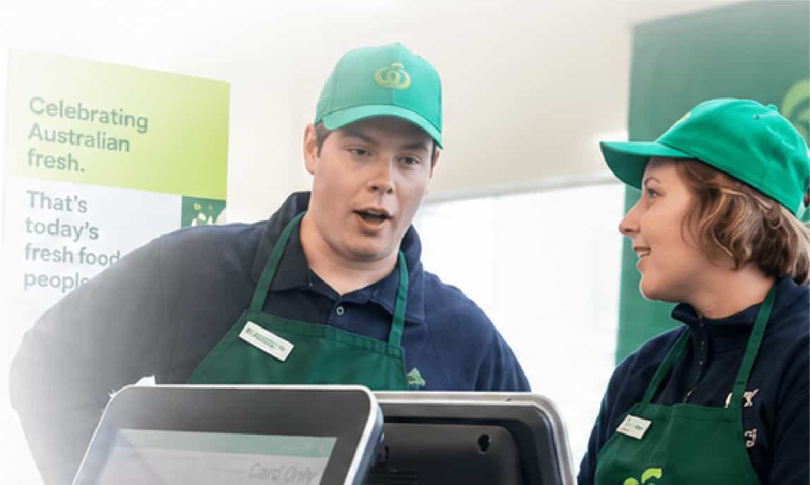 Two staff in green uniforms and caps speaking beside a counter in a bright office setting