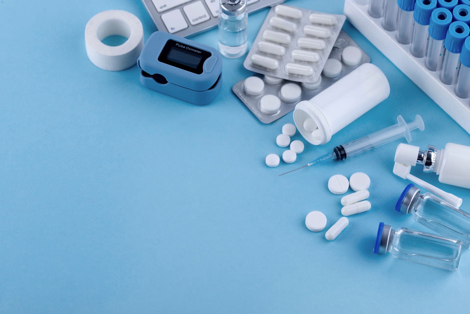 A blue table topped with a variety of medical supplies including pills , syringes , and a keyboard.