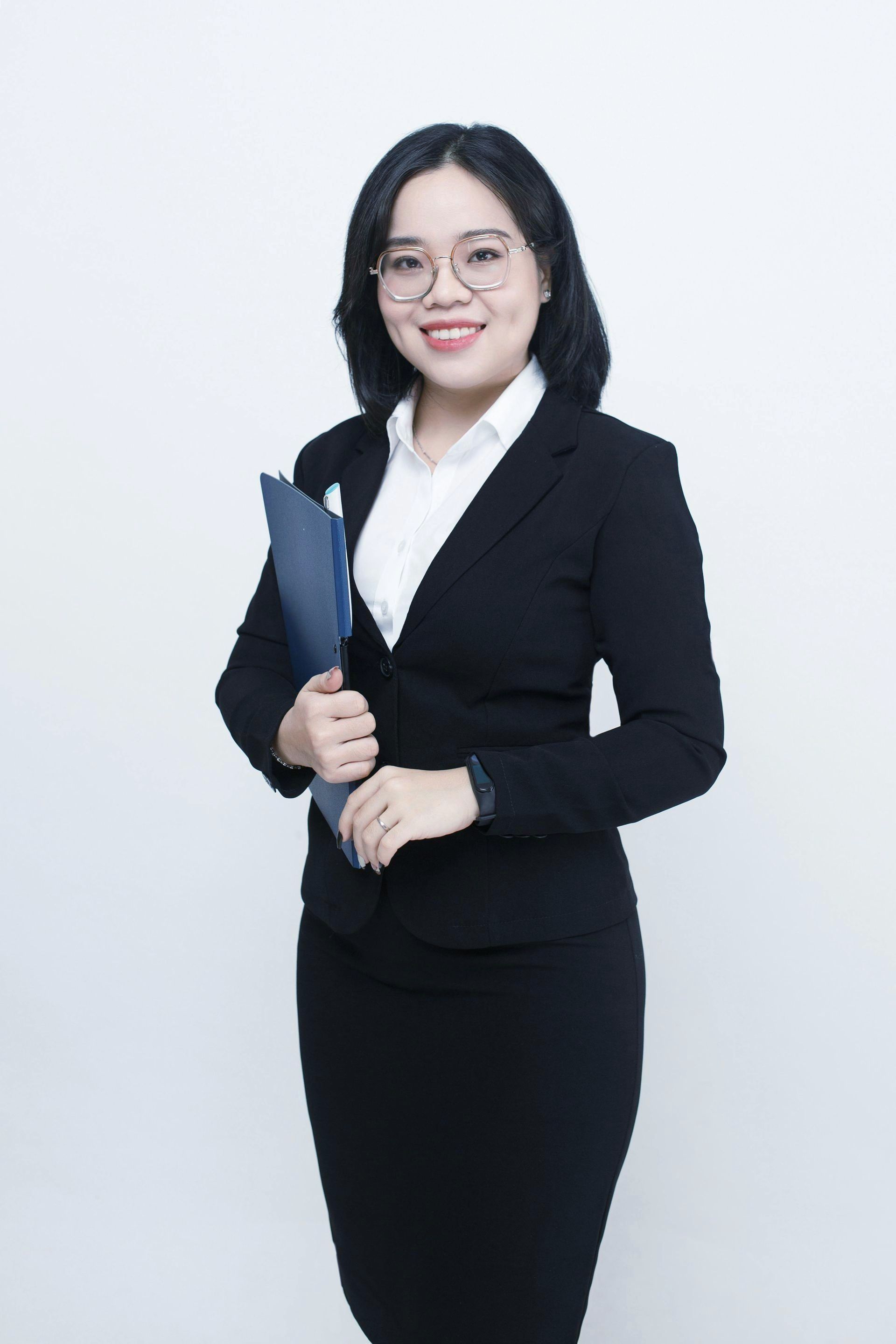 A woman in a black suit and glasses is holding a folder.