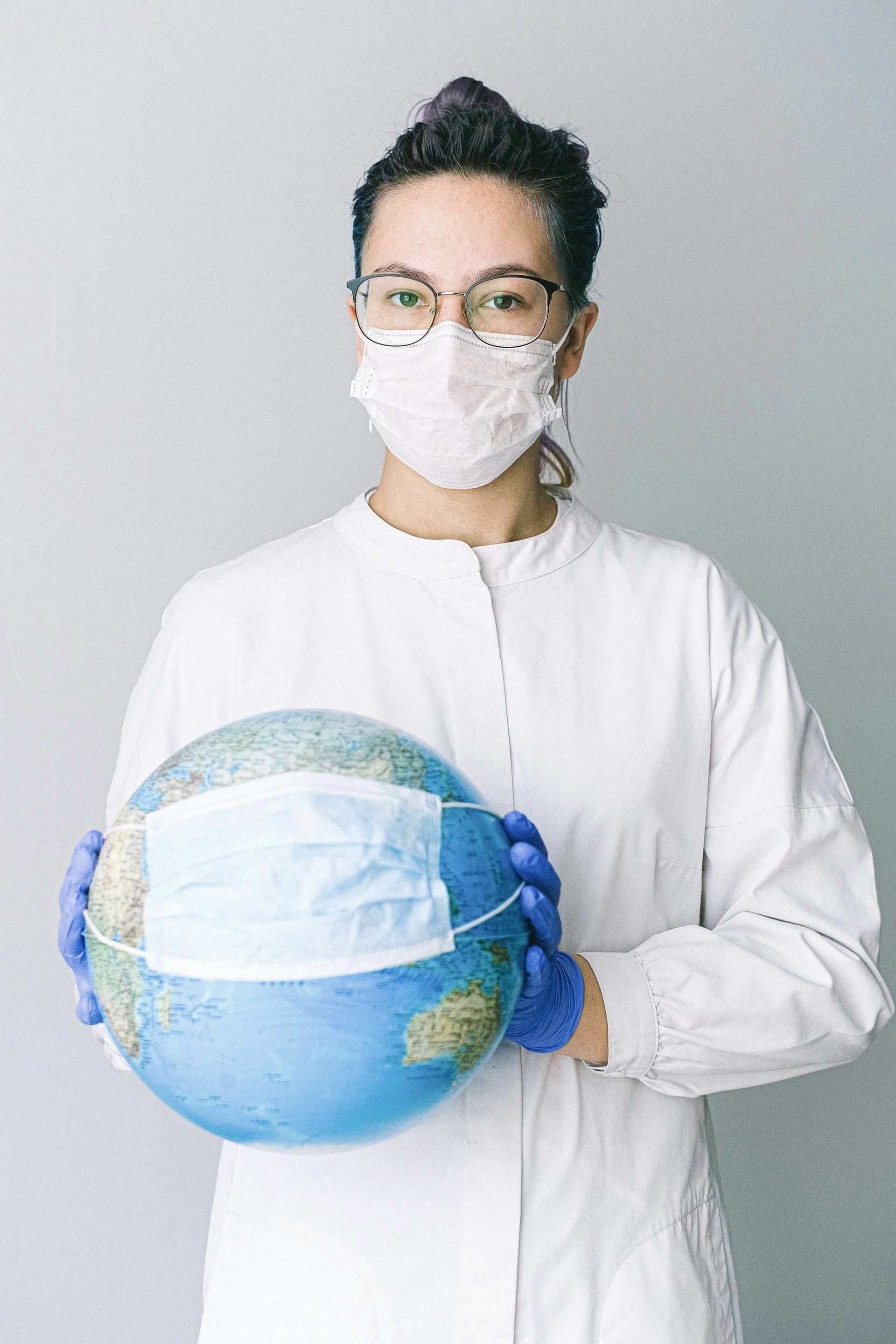 A woman wearing a mask and gloves is holding a globe.