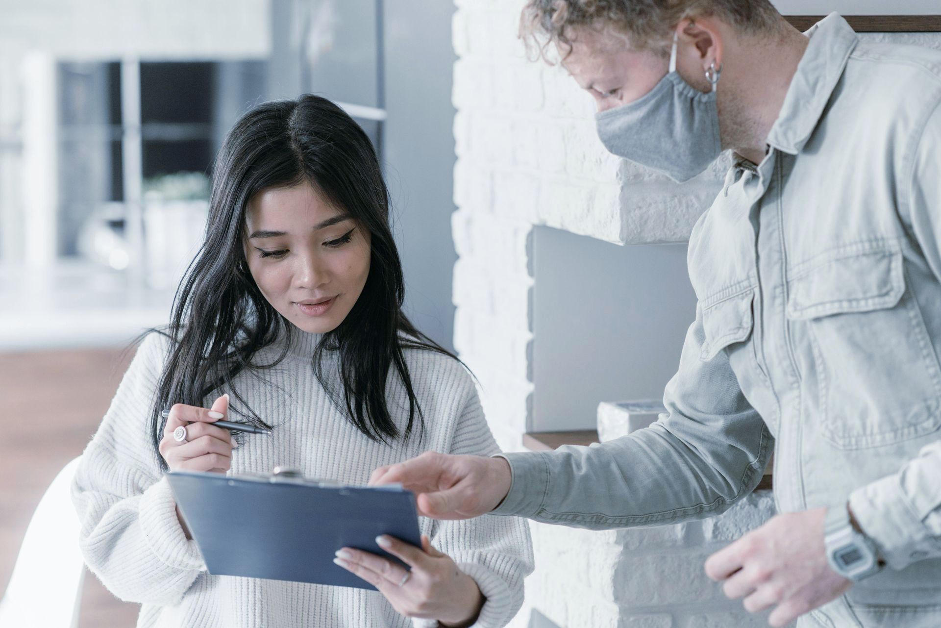 A man and a woman wearing face masks are looking at a clipboard.