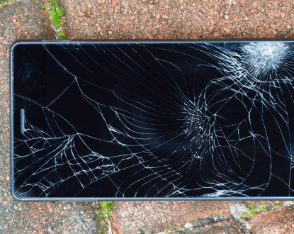 A cell phone with a broken screen is laying on the ground