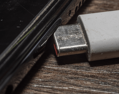 A close up of a charger plugged into a cell phone on a wooden table.
