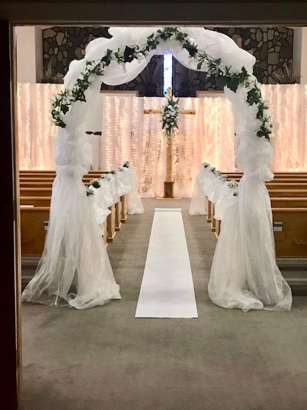 A church decorated for a wedding with a white arch and a white aisle.