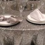 A table with plates , napkins , glasses and a silver table cloth.