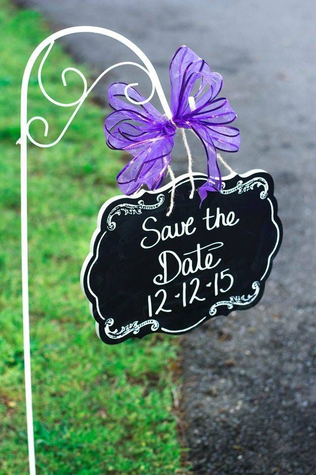 A save the date sign with a purple flower attached to it.