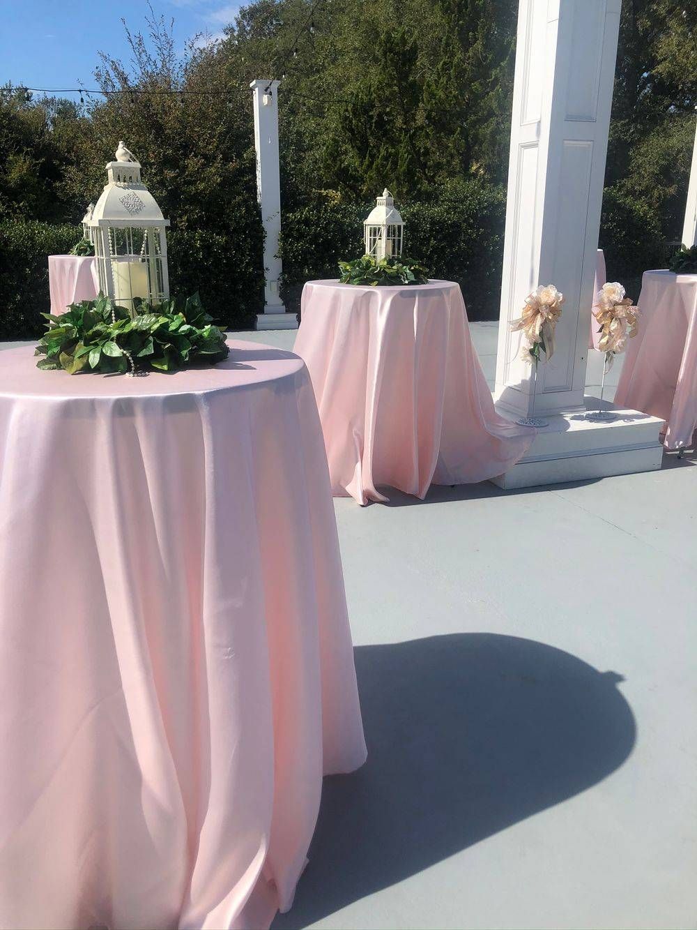 A row of tables with pink linens and lanterns on them