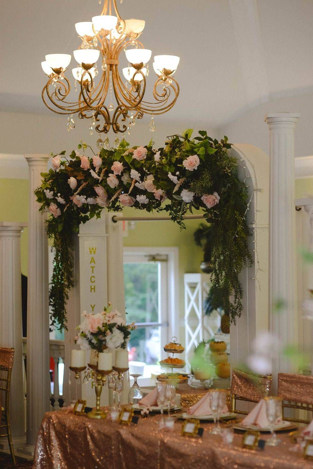 A long table with a chandelier hanging from the ceiling and flowers on it.