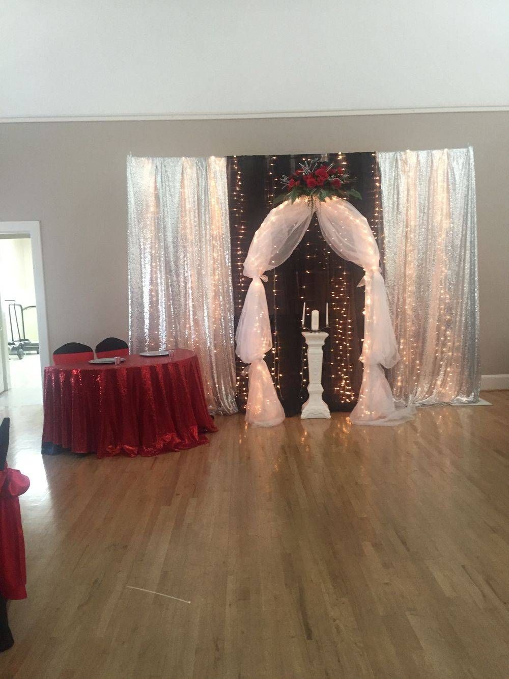 A room with a table and chairs in front of a wedding arch.