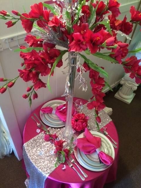 A table with plates and silverware and a vase of red flowers