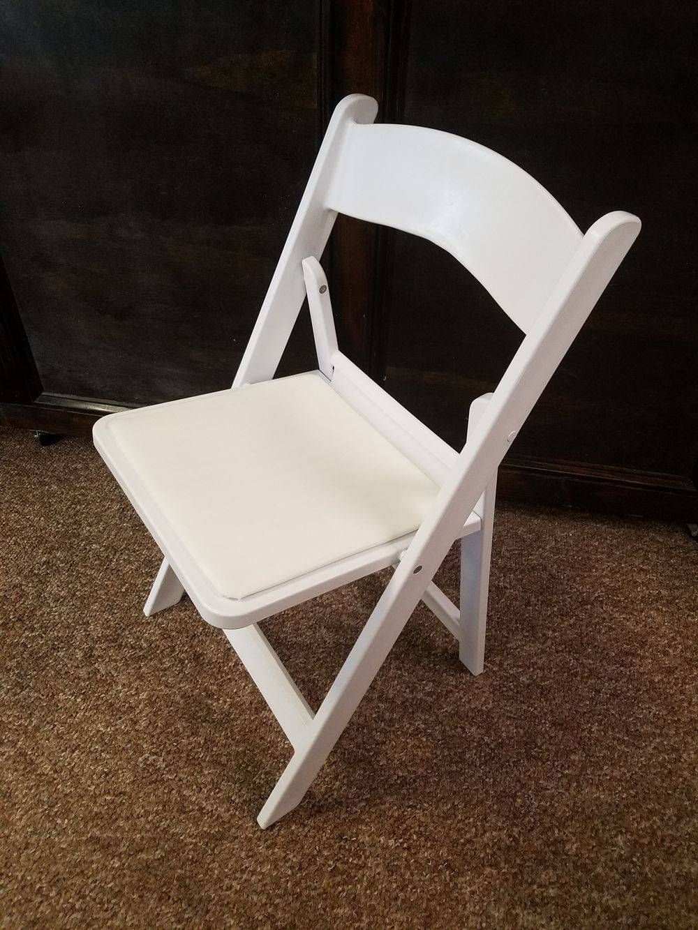 A white folding chair with a white cushion is sitting on a carpet.