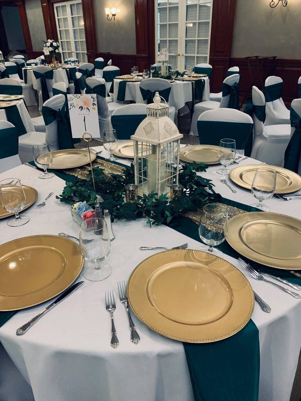 A table set for a wedding reception with gold plates and green napkins.