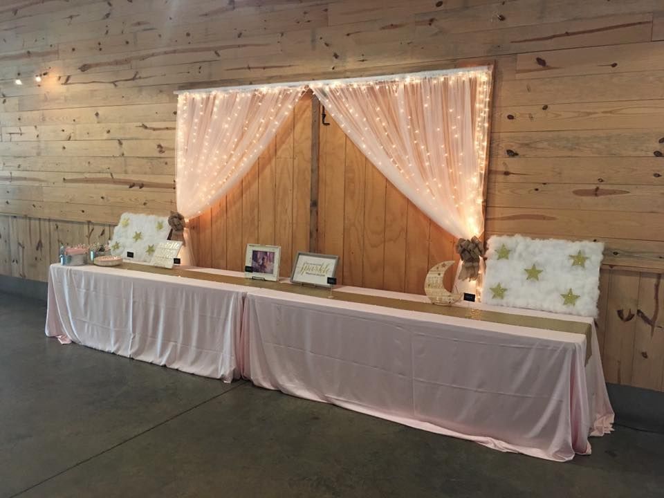 A long table with a pink tablecloth is sitting in front of a wooden wall.
