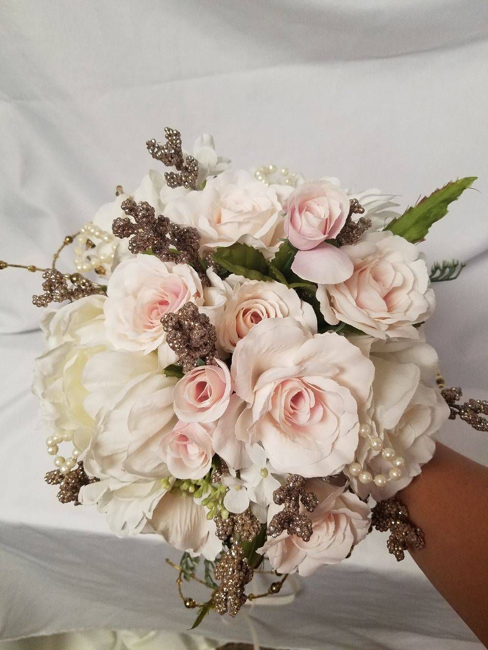 A person is holding a bouquet of pink and white flowers on their wrist.