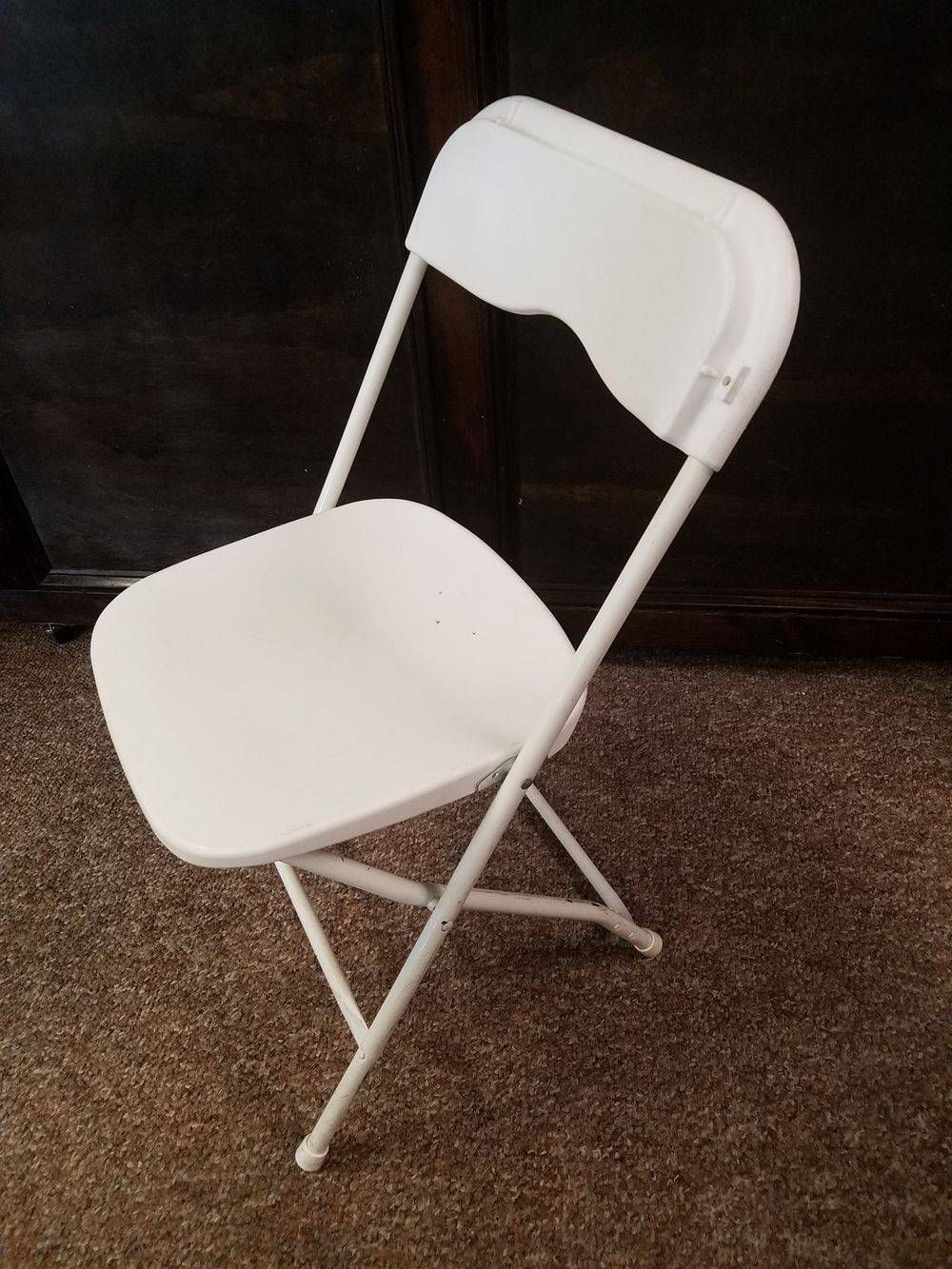 A white folding chair is sitting on a brown carpet.