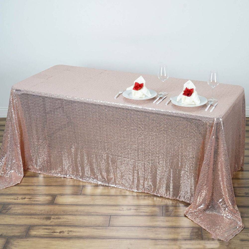 A table with plates and silverware on it and a rose gold sequined tablecloth.