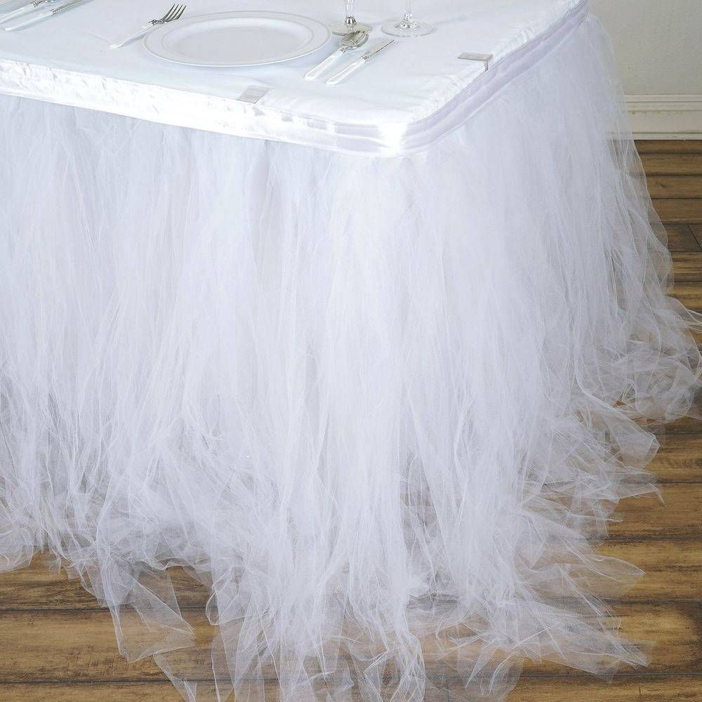 A white tulle table skirt is sitting on top of a wooden table.
