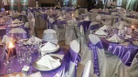 A room filled with tables and chairs decorated in purple and white for a wedding reception.