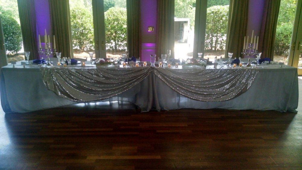 A long table with a white table cloth and candles on it in a room.