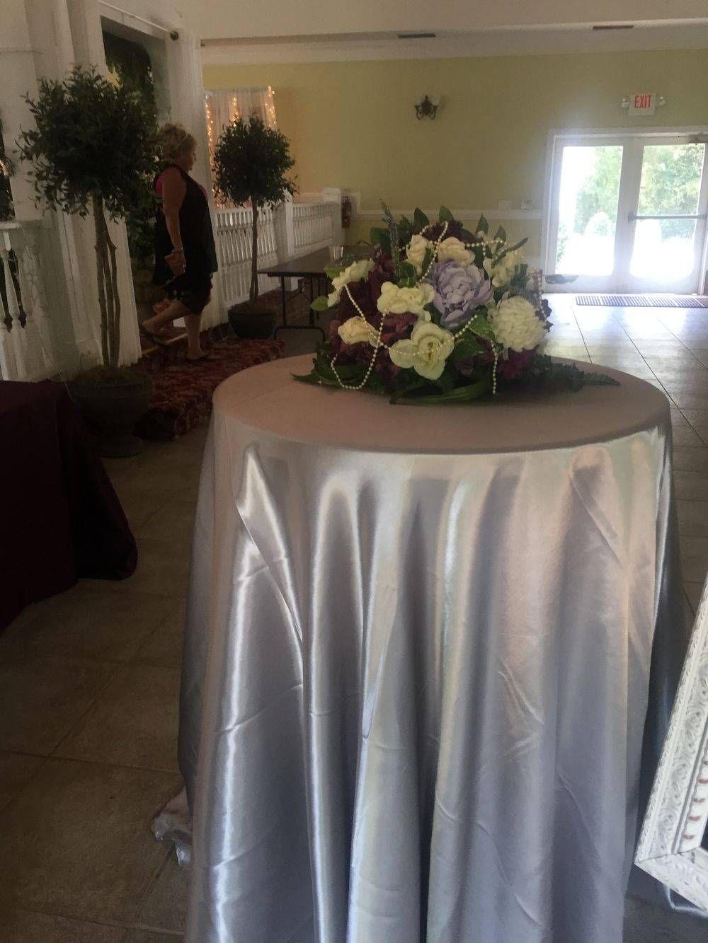 A table with a silver tablecloth and flowers on it.