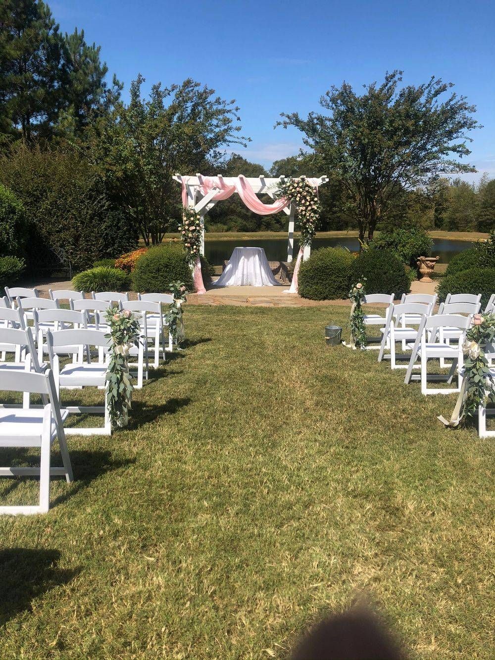 A row of white chairs are lined up in a grassy field in front of a wedding arch.