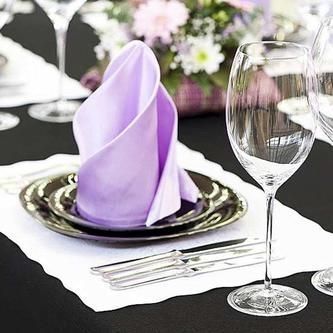 A table setting with plates , utensils , wine glasses and a purple napkin.