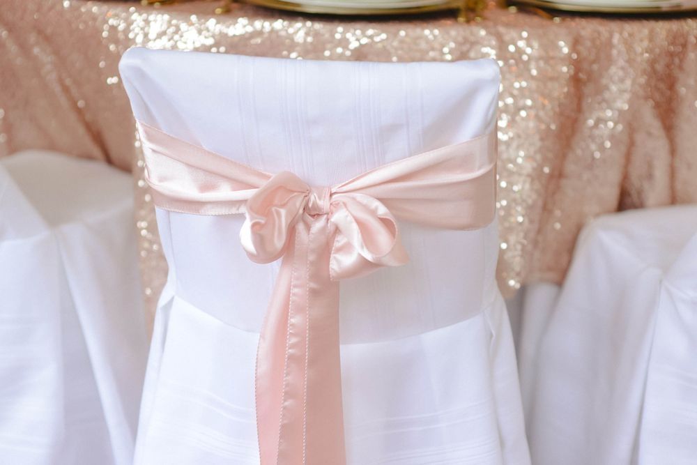 A white chair with a pink satin sash is sitting at a table.
