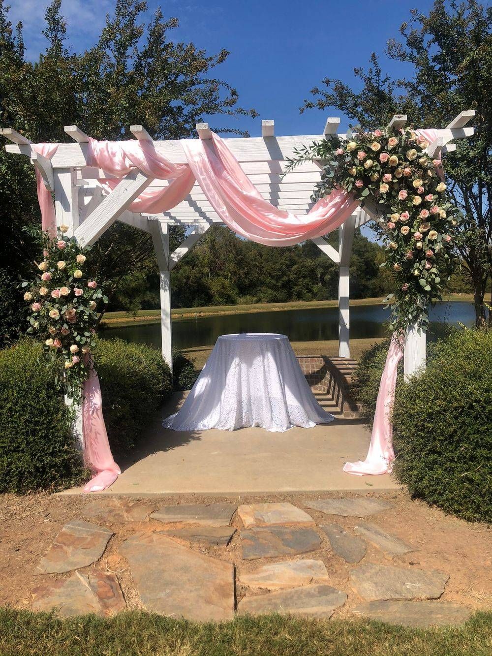 A white pergola with pink flowers and a table underneath it.