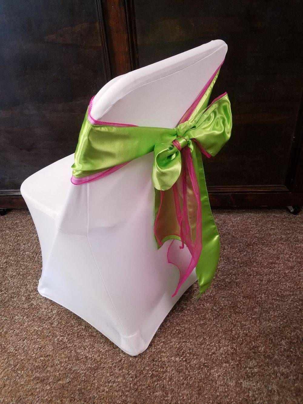 A white chair with a green and pink bow on it.