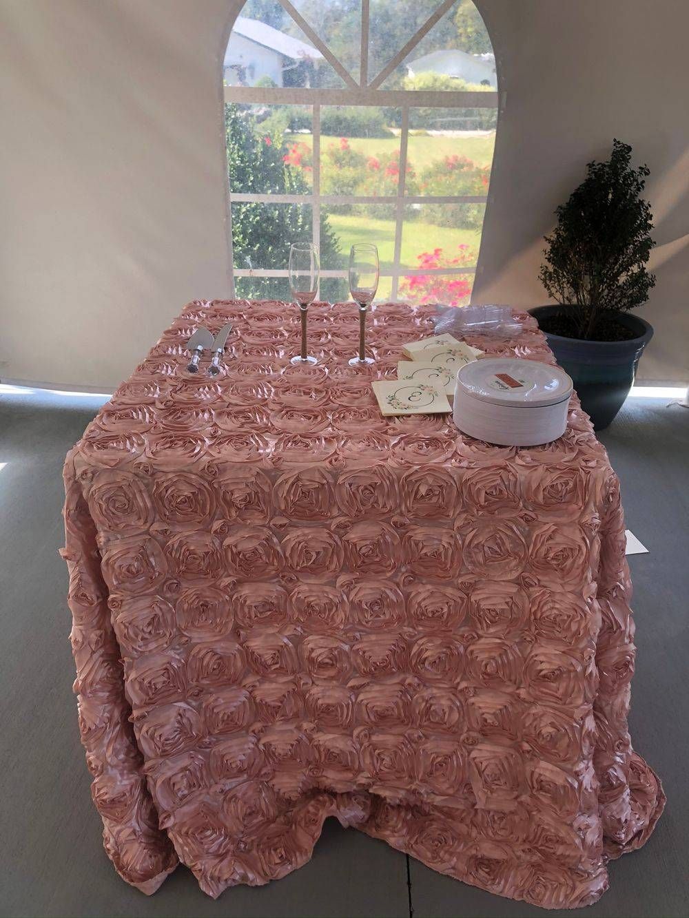 A table with a pink tablecloth and glasses on it in front of a window.