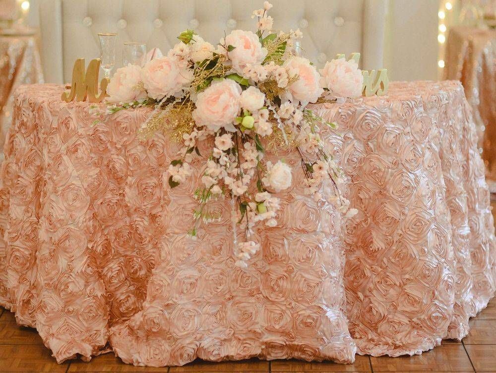 A table with a rose gold tablecloth and flowers on it.