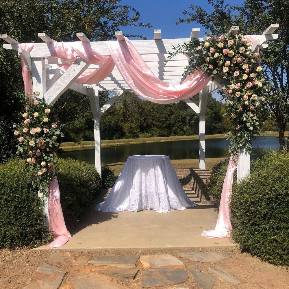 A white pergola with pink flowers and a table underneath it