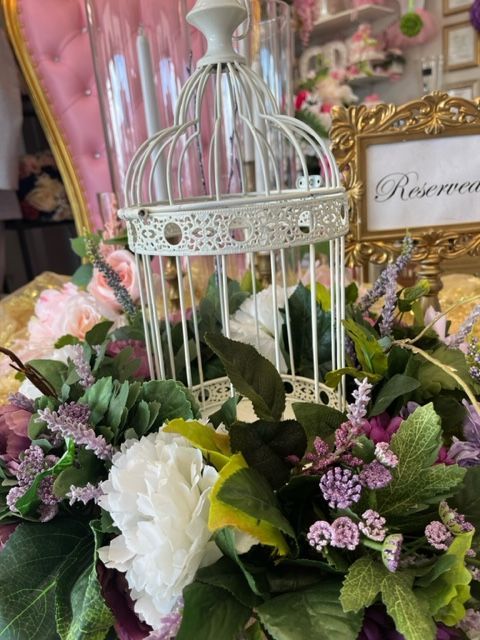 A white bird cage is surrounded by flowers on a table.