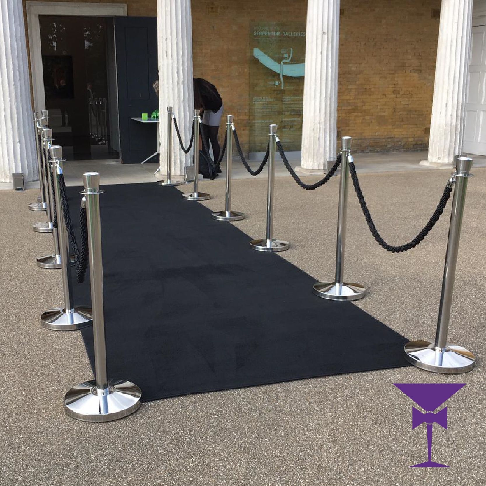 A black carpet is lined up with rope barriers in front of a building