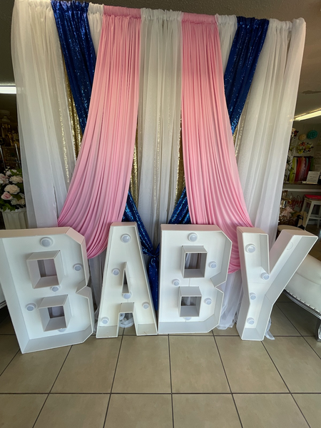A baby shower backdrop with a baby sign in front of a pink and blue curtain.