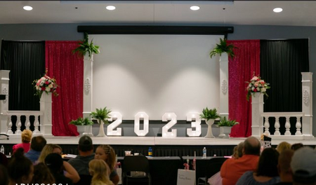 A group of people are sitting in front of a stage with the numbers 2023 on it.