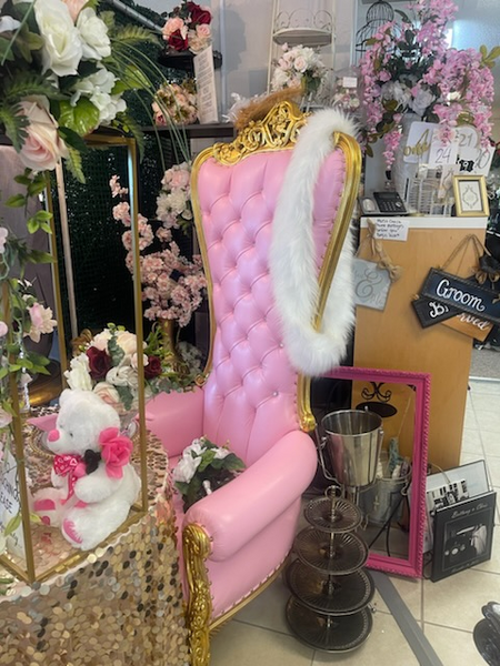 A pink and gold chair is surrounded by flowers and a sign that says groom