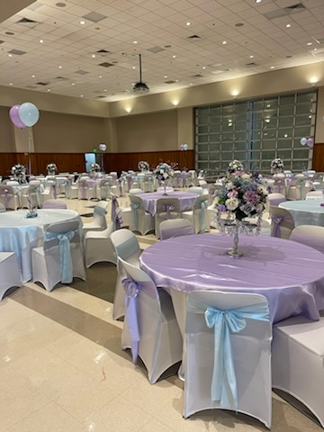 A large room filled with tables and chairs decorated for a wedding reception.