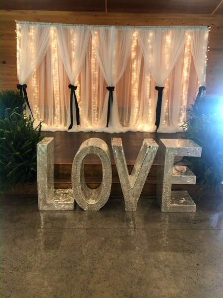 A large love sign is sitting in front of a white curtain.