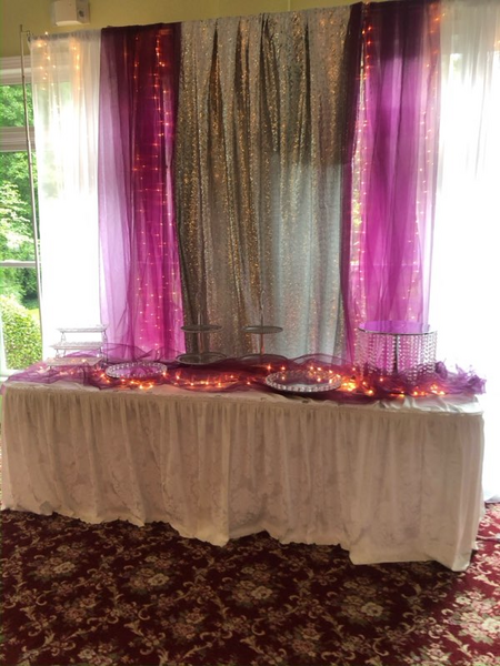 A table is sitting in front of a window with purple and silver curtains.