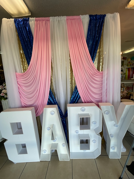 A baby shower backdrop with a baby sign in front of a pink and blue curtain.