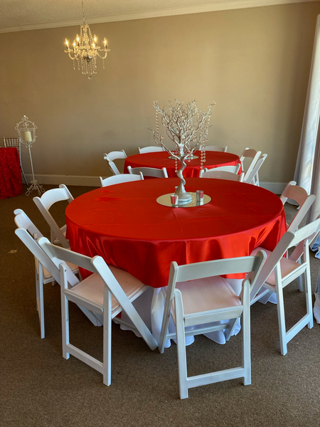 A round table with a red table cloth and white chairs