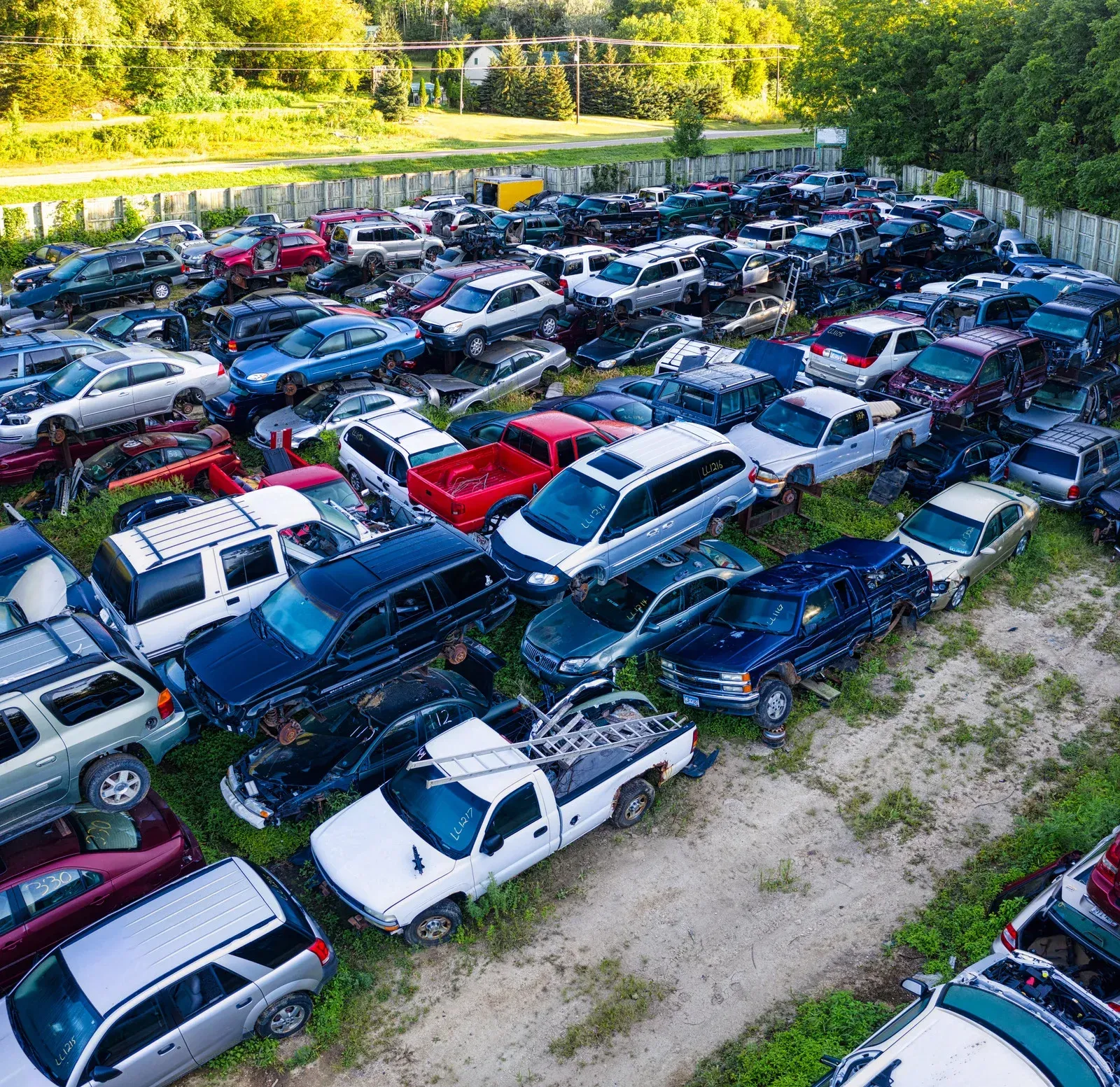 Overhead view of a junkyard filled with numerous parked cars of various makes and colors.
