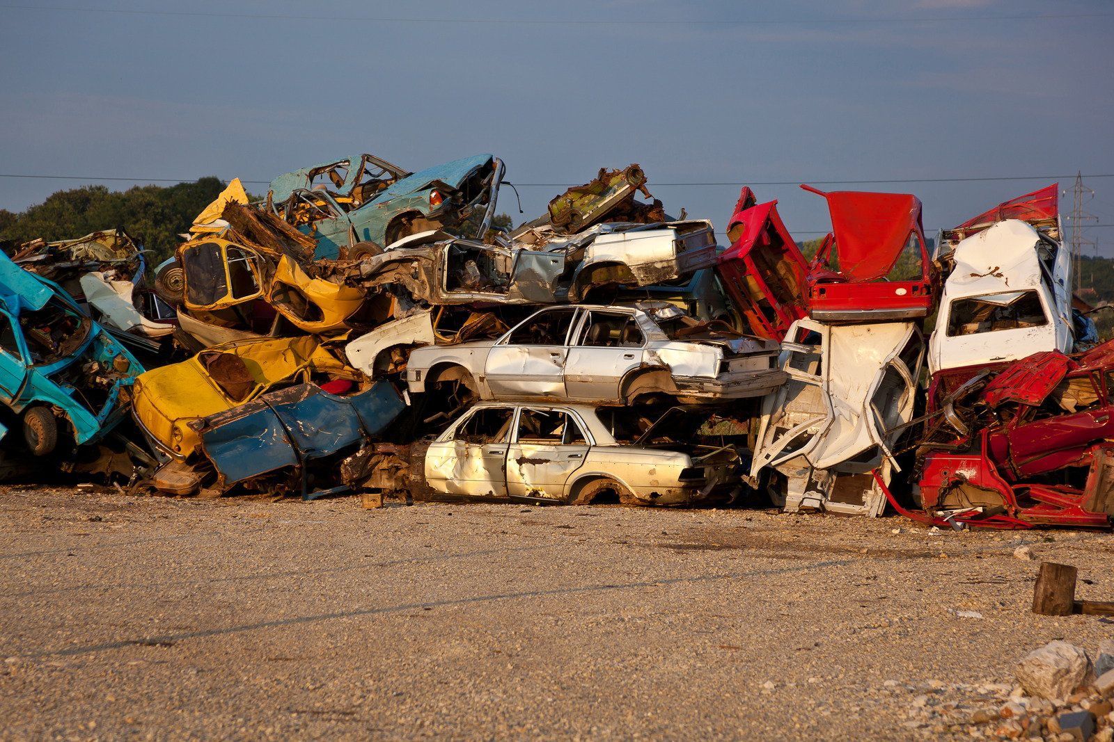 Pile of colorful, crushed cars at a junkyard; blue, yellow, red, and white vehicles are stacked.