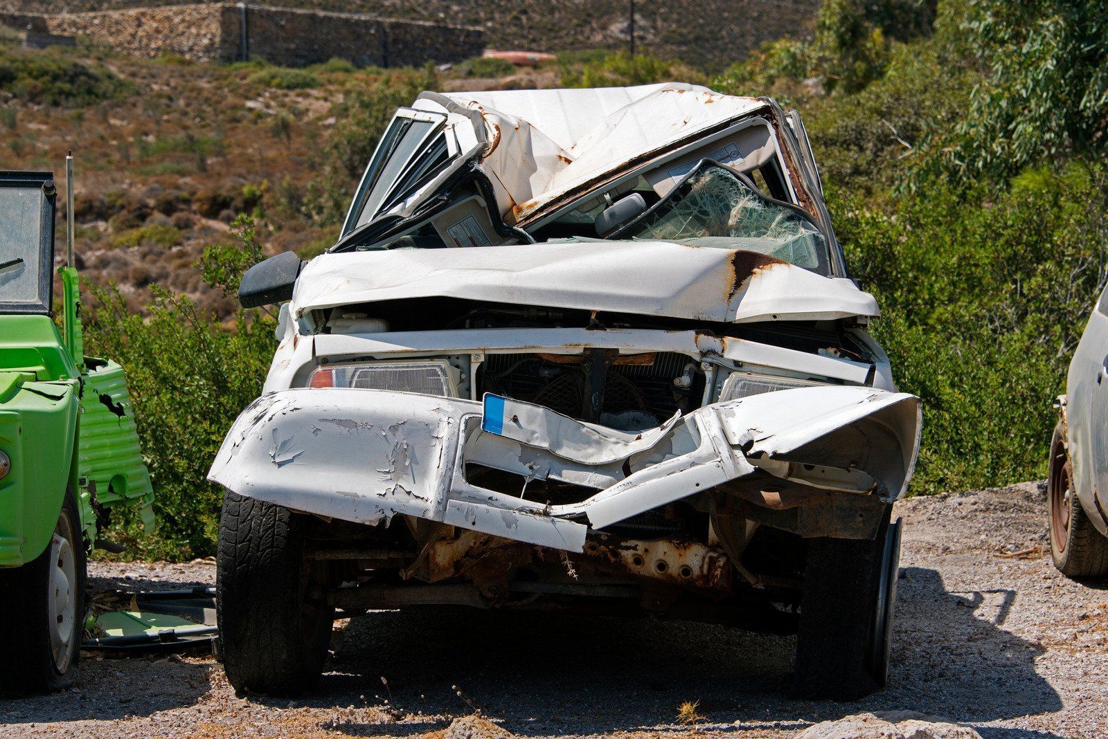 A severely damaged white SUV, crushed front, parked outdoors near greenery.